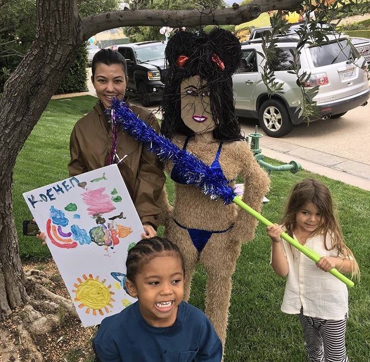 Kourtney Kardashian stands next to her birthday pinata as her nephew Saint and son Reign, right ...
