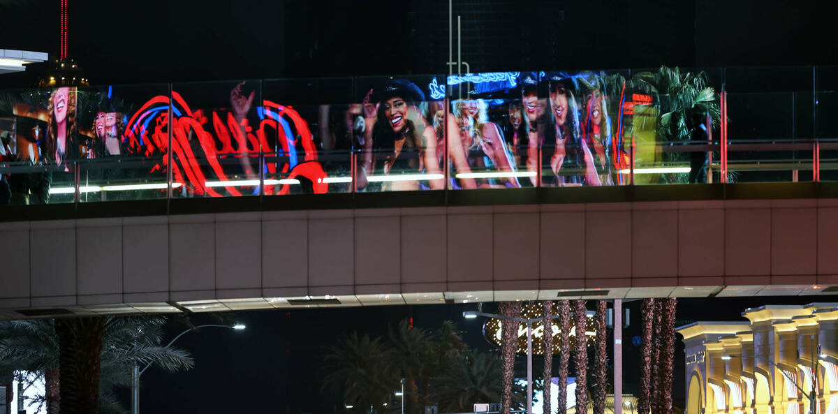 Pedestrians walk along a bridge over S. Las Vegas Blvd. as an ad is reflected on the glass alon ...