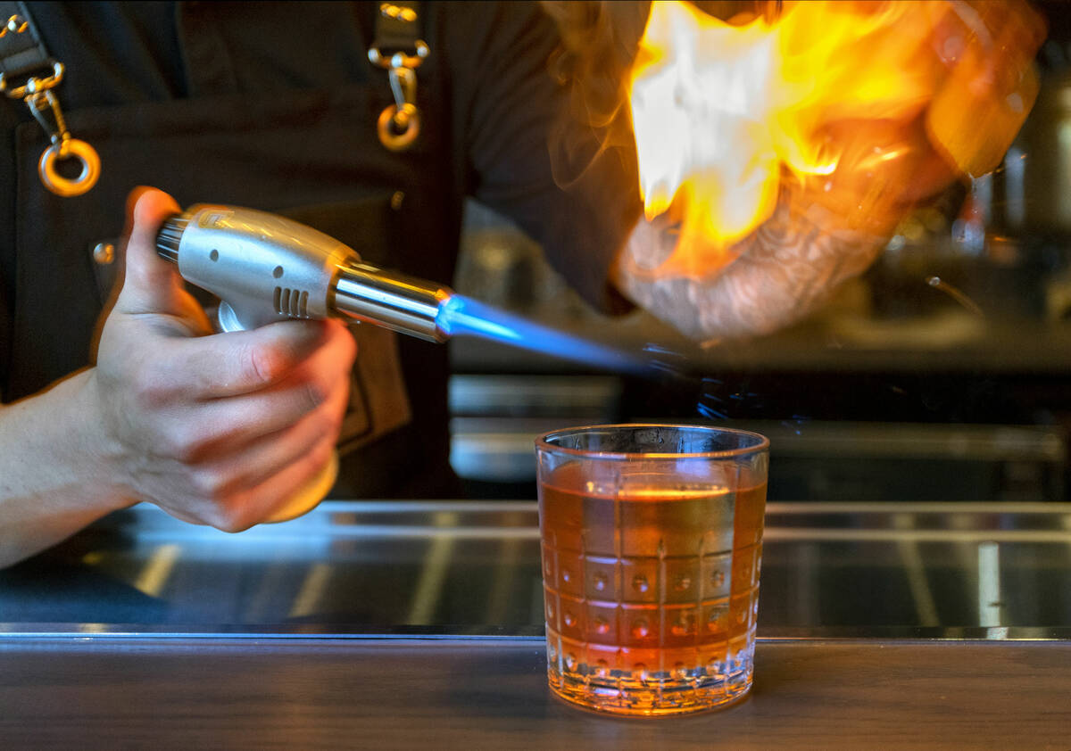 Bartender Riki Taiga singes a garnish for an Old Fashioned cocktail about The Lock hidden speak ...
