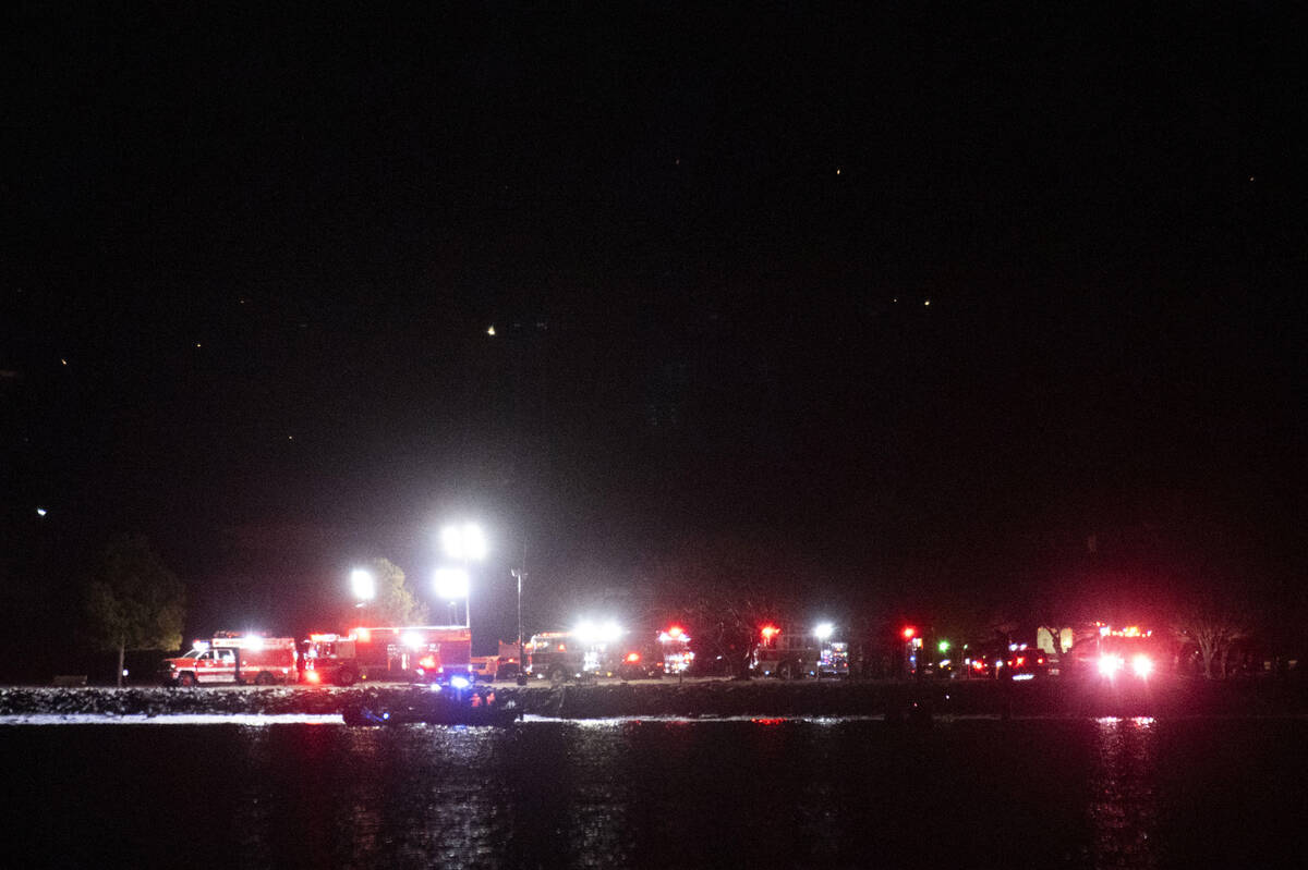 A boat on the Potomac River, cruises past emergency response vehicles seen staging at Joint Bas ...