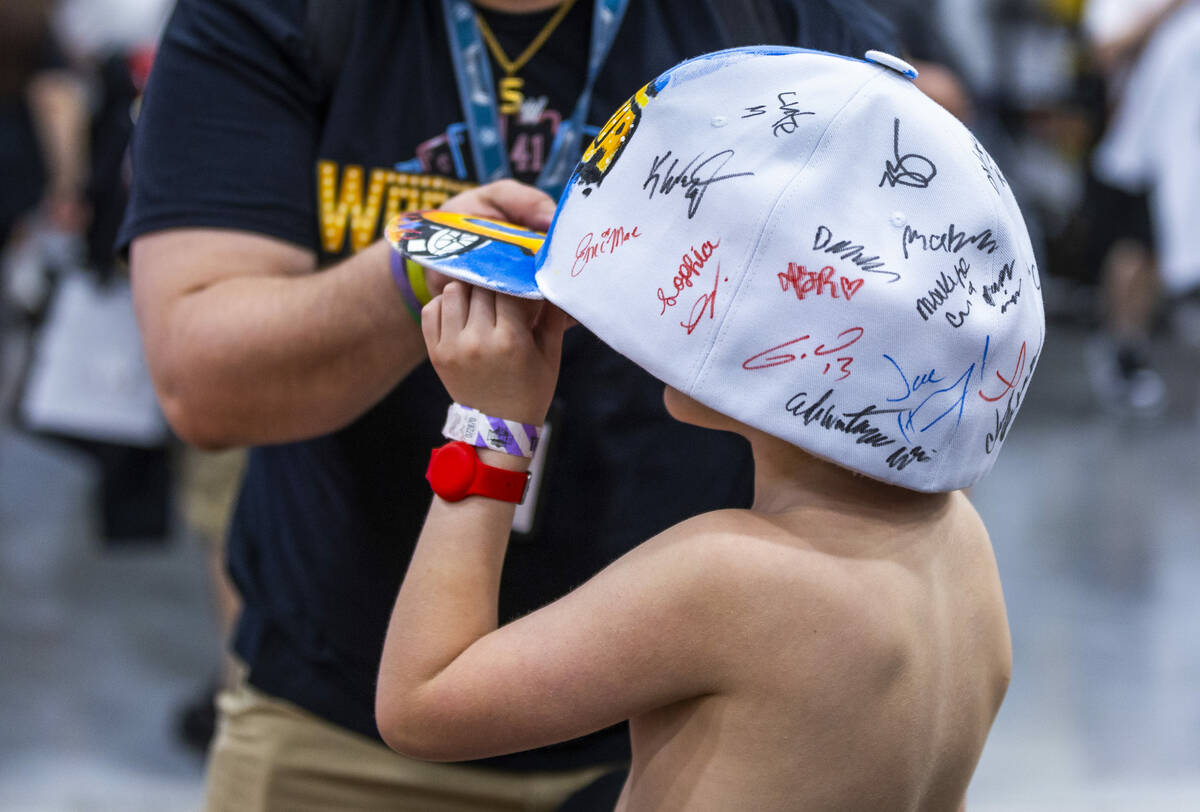 A young fan tries on a large hat adorned with autographs at the WrestleMania Superstore within ...