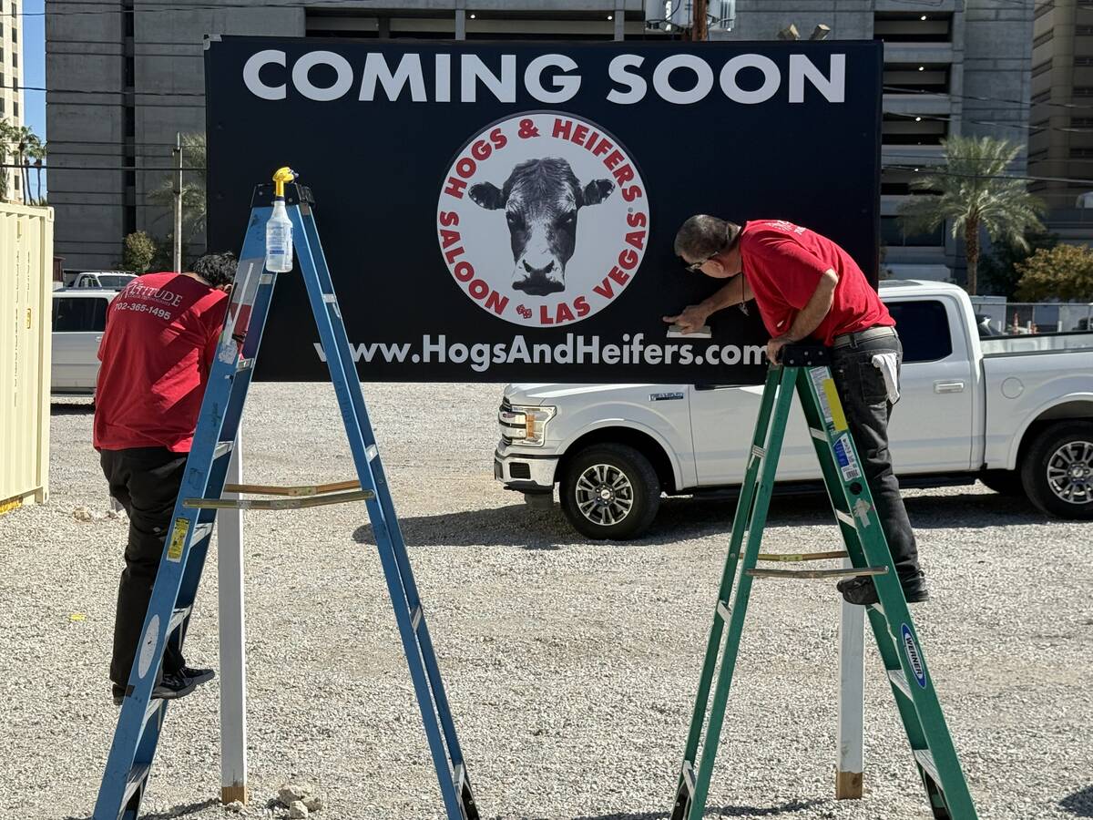 A pair of workers finish installing the new, temporary sign just installed at the new Hogs & H ...