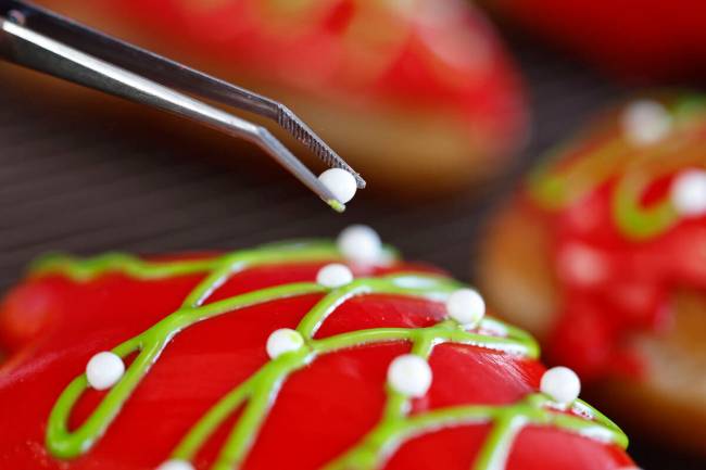 Robert Teddy puts the finishing touches on a Christmas-themed doughnut at his west valley shop. ...