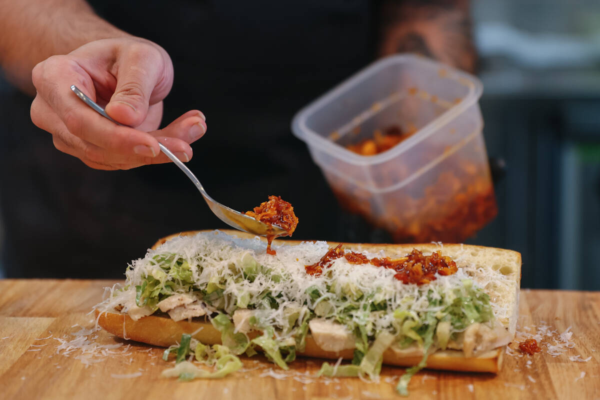 Scott Arn spoons homemade chili crisp over a chicken sandwich at Golden Boy Market & Deli on Tu ...
