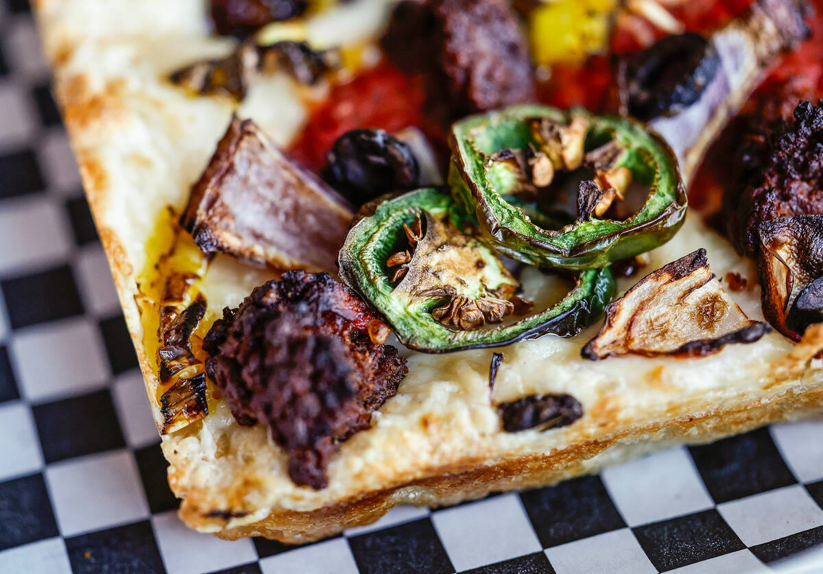 A vegan pizza with vegan cheese, vegan sausage, jalapeño, red onion and black olive is see ...