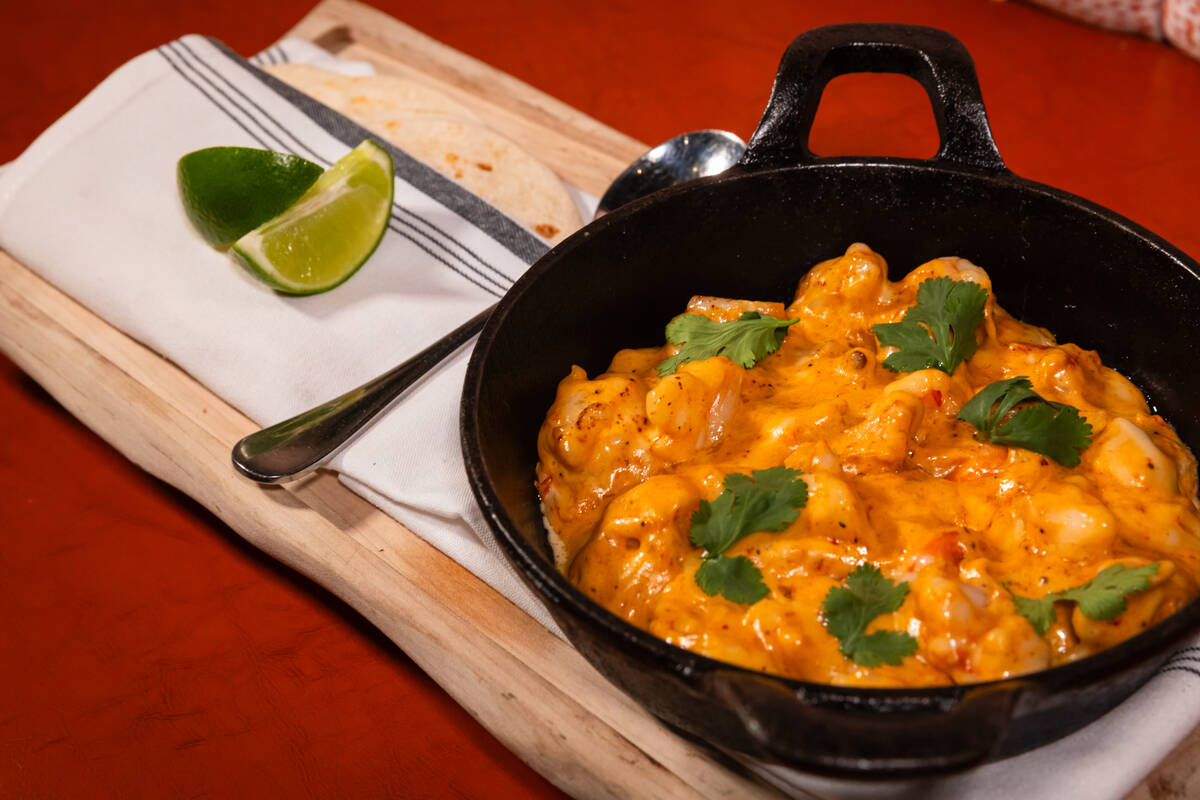 A cast-iron skillet of shrimp in a creamy orange sauce with fresh herbs and lime wedges at Boom Bang Fine Foods and Cocktails