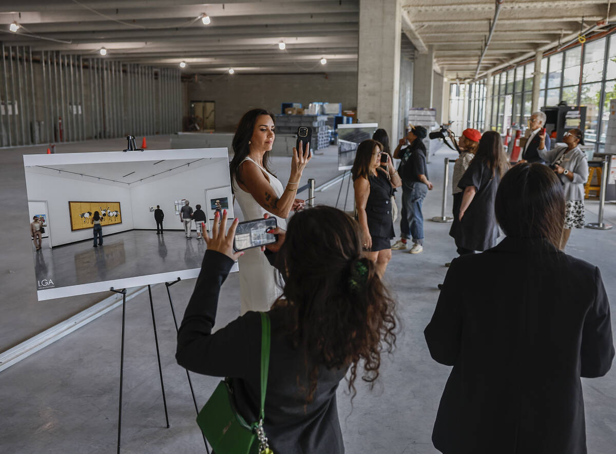 Visitors take photos inside the unfinished concrete interior of Grand Central Galleries, next to an easel showing a rendering of a finished white-walled gallery